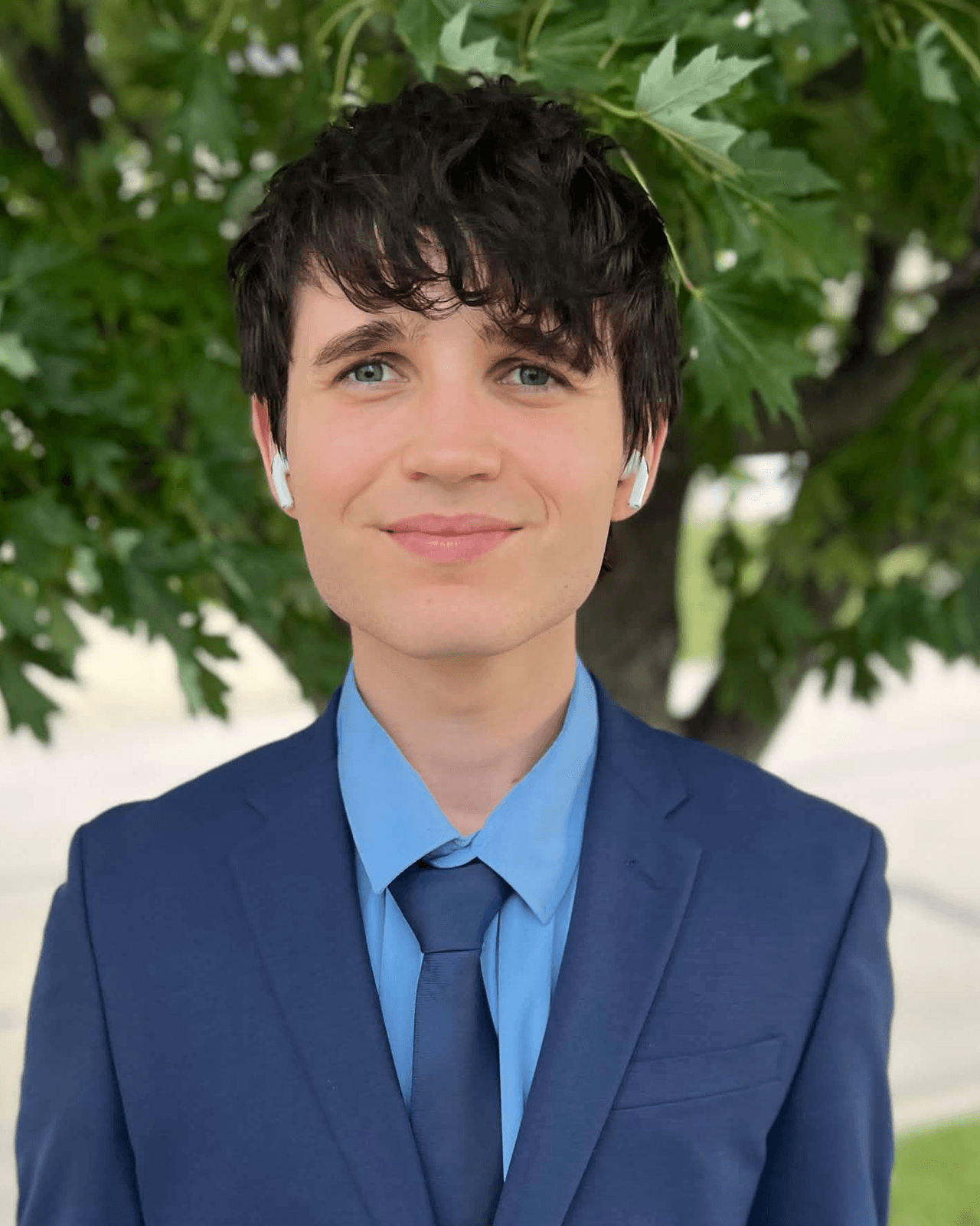 Jaden Flanery in a navy suit and tie, photographed outdoors under a tree